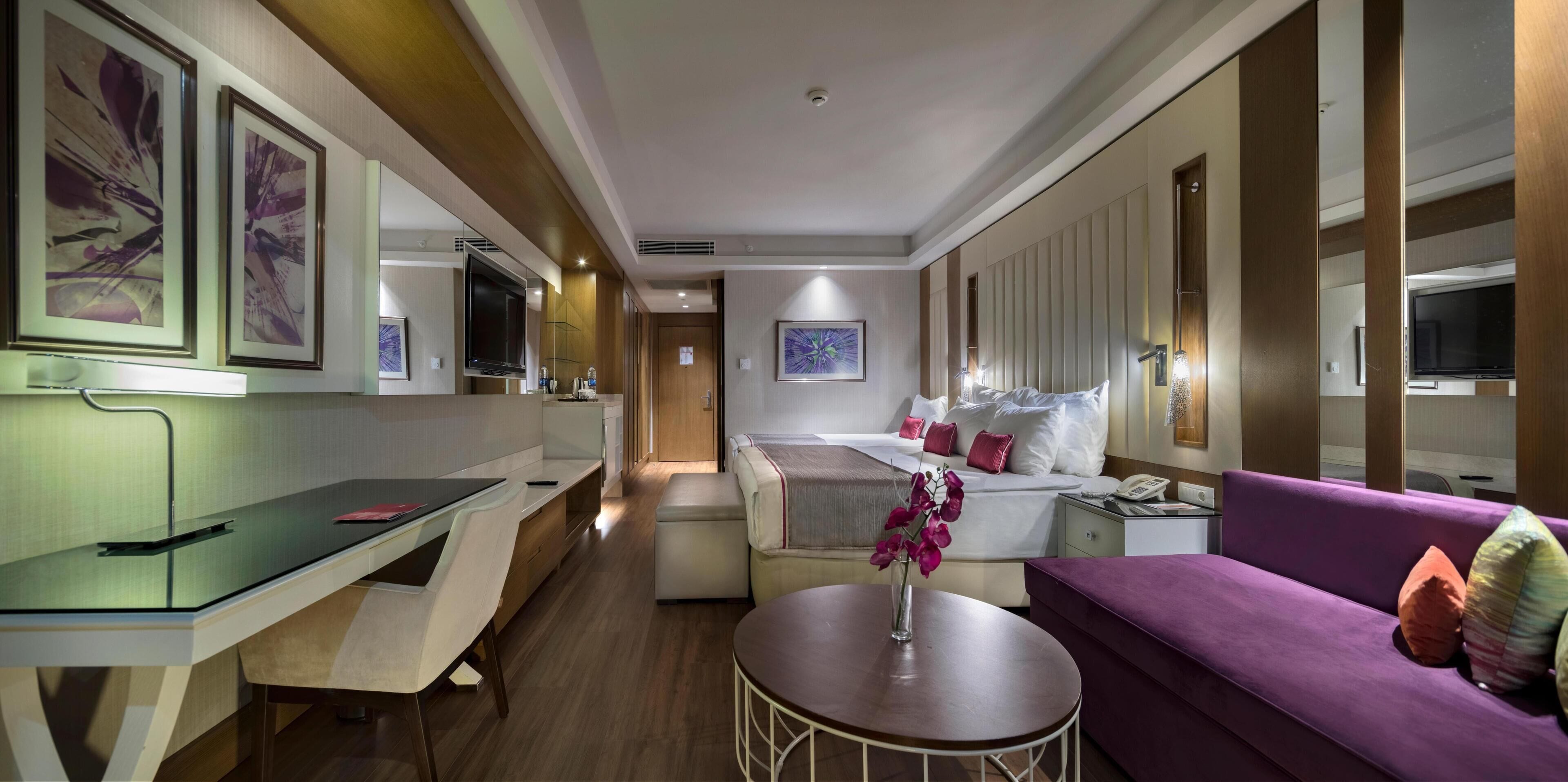 Habitación de hotel con cama, sofá, escritorio y una pequeña mesa con un florero.