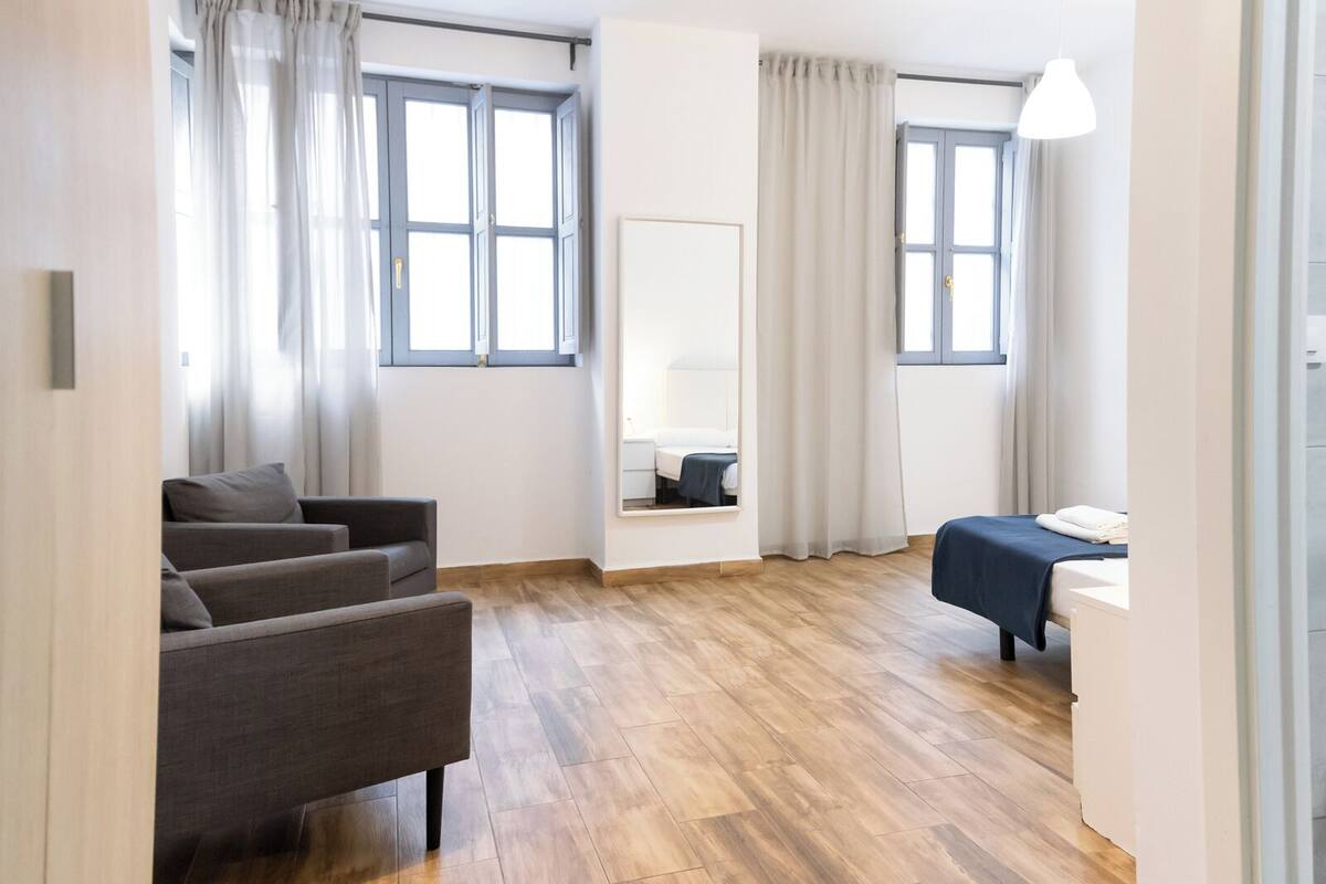 Une pièce moderne et bien éclairée, avec un plancher en bois, un canapé, un lit et un miroir.