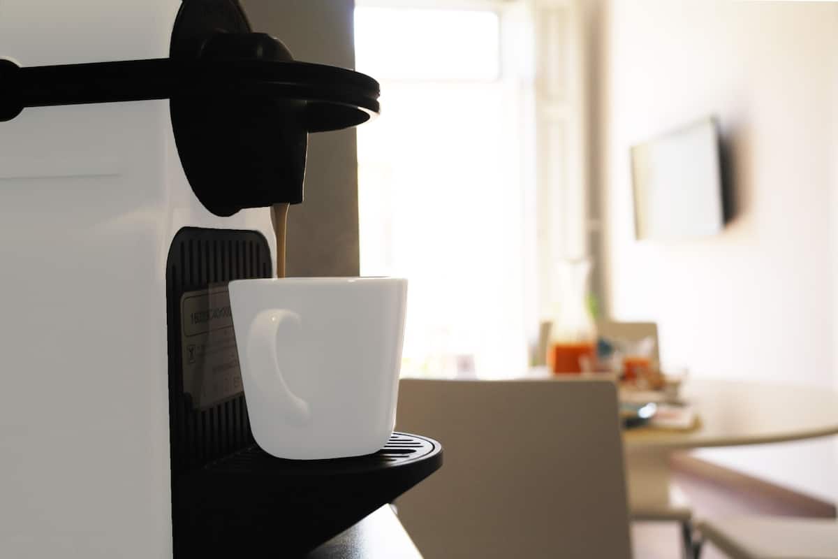 Une machine à café avec une tasse posée sur le bac d’égouttement, une fenêtre en arrière-plan et un téléviseur à écran plat accroché au mur.