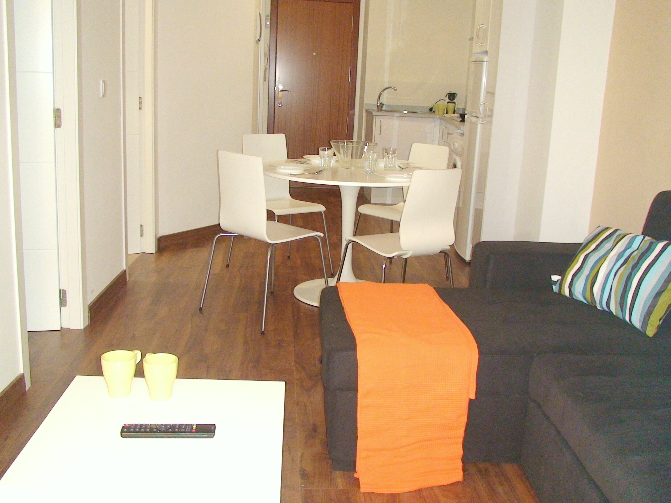 Ein Wohnzimmer mit einer schwarzen Couch, einem weißen Couchtisch und einem Essbereich mit einem weißen Tisch und Stühlen.