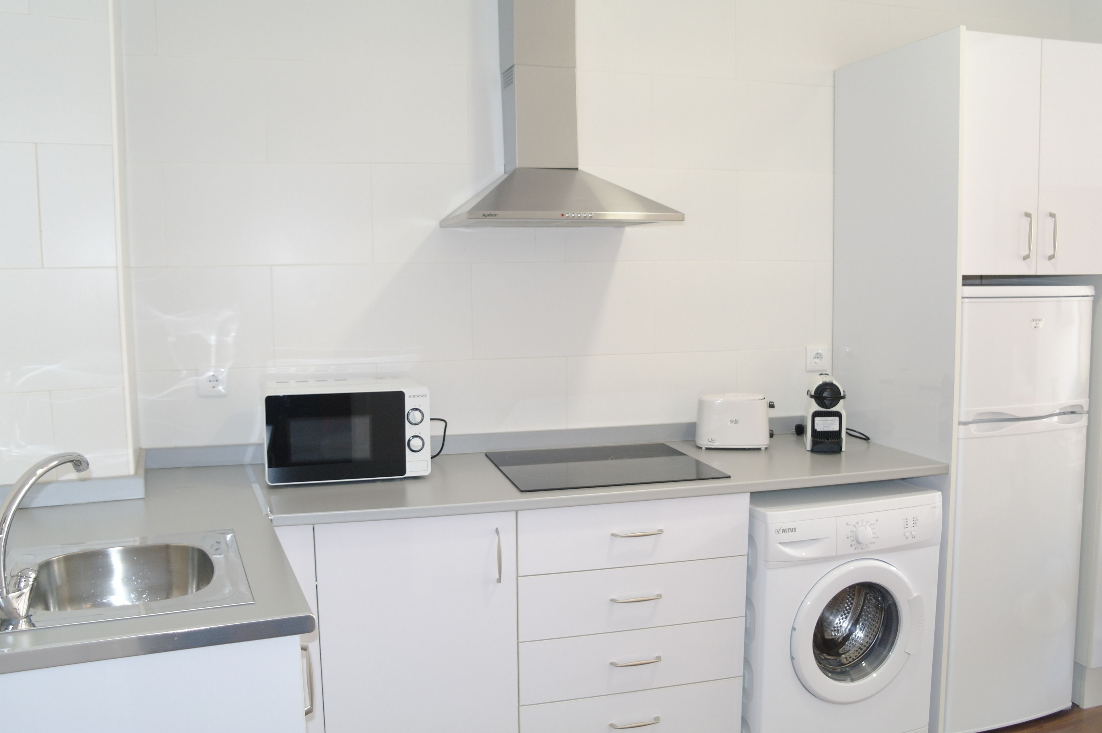 A modern kitchen with white cabinetry, a stainless steel sink, a microwave, a toaster, a coffee maker, and a dishwasher.