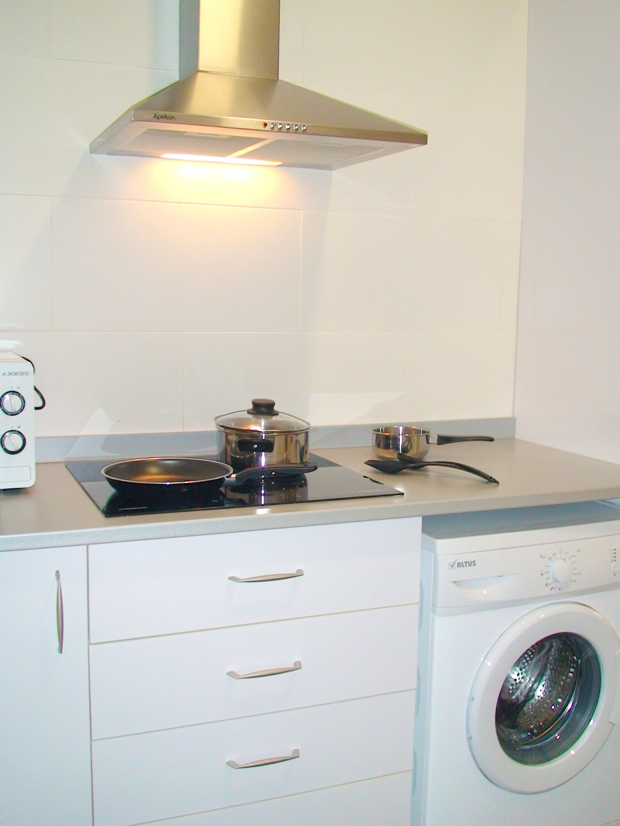 A compact kitchen with a stove, pots, a microwave, and a built-in washing machine.