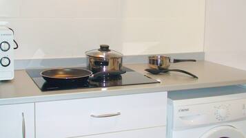 A compact kitchen with a stove, pots, a microwave, and a built-in washing machine.