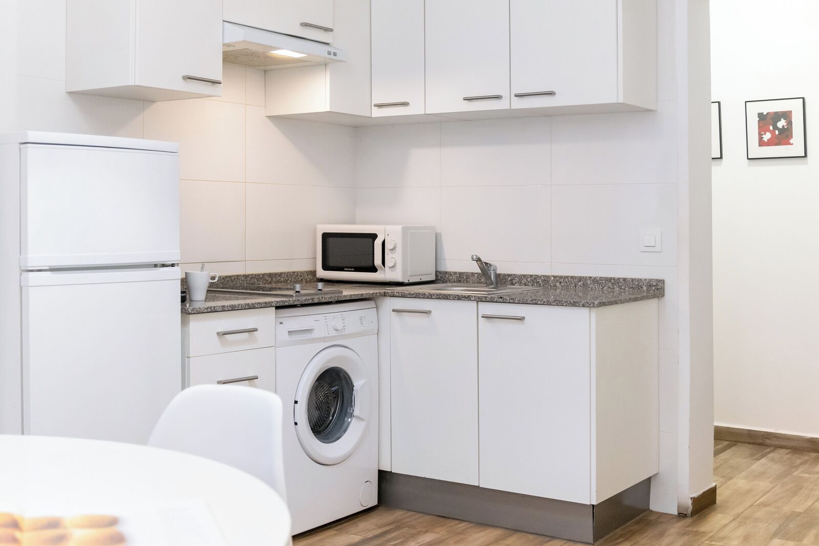 Een kleine keuken met een wasmachine, magnetron en een eethoekje.