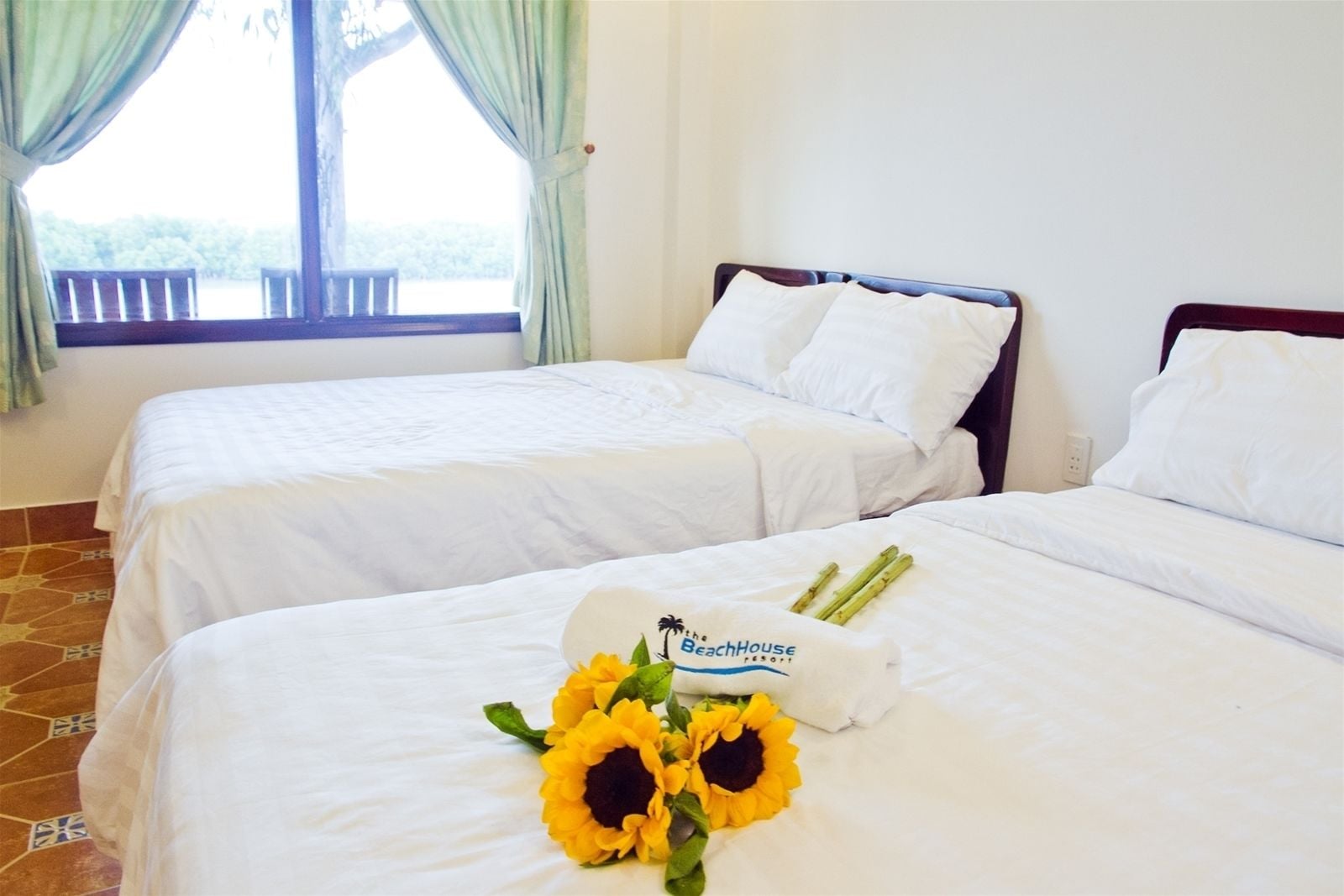 Two single beds in a hotel room with white bedding and a window with curtains.
