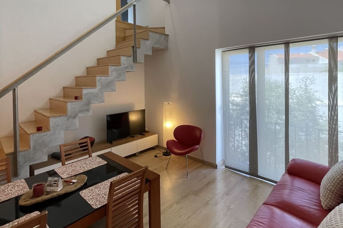 A modern living space with a staircase, dining area, and a red sofa.