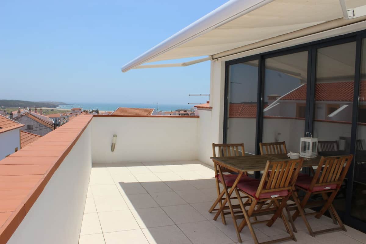 A balcony with a table and chairs, a view of the sea, and a tiled floor.
