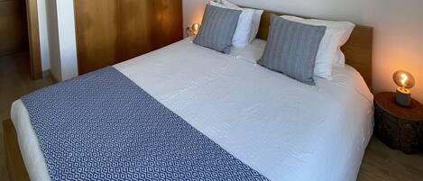 A bedroom with a large bed, wooden wardrobe, and bedside lamps.