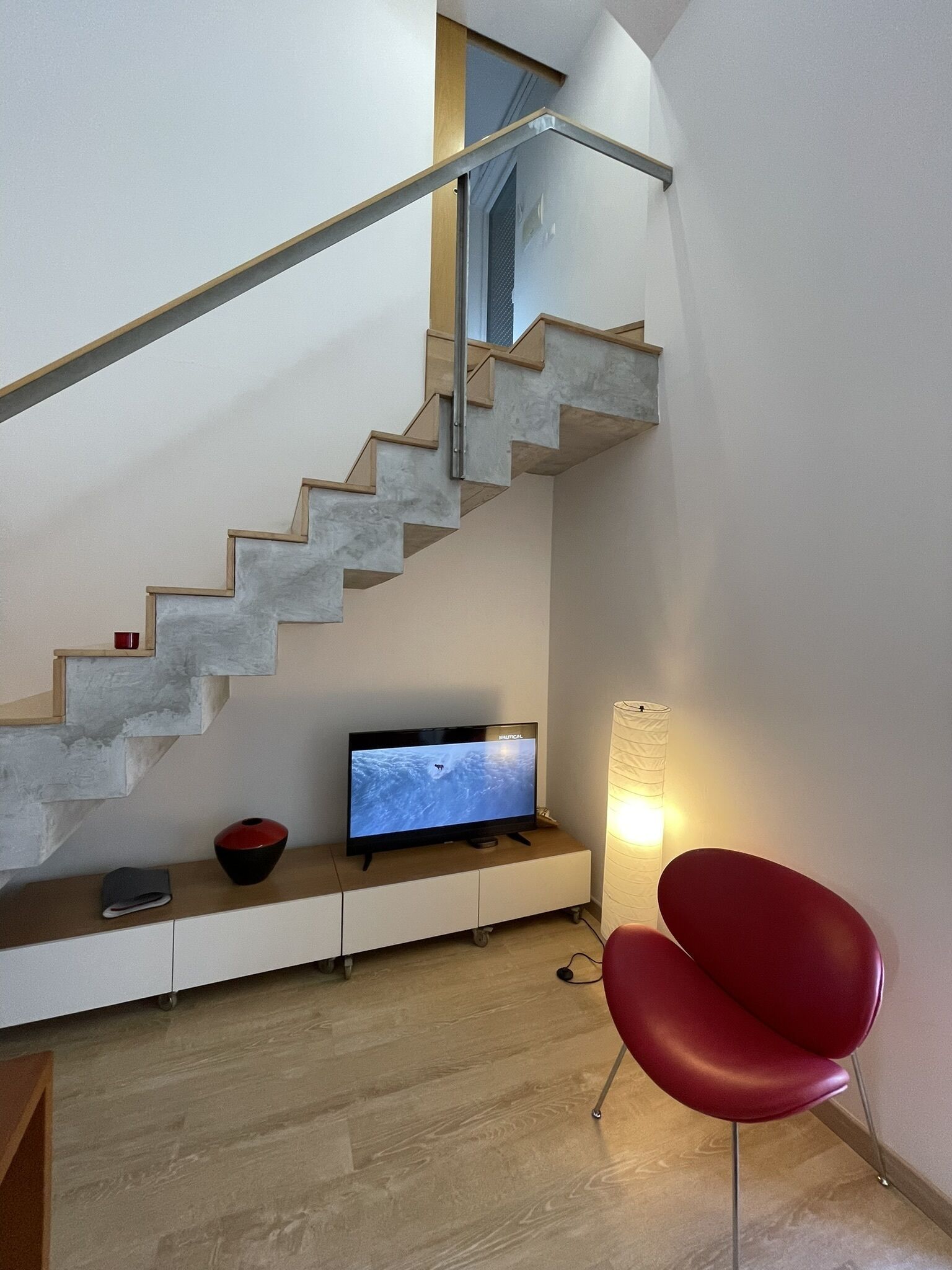 Un intérieur moderne avec un escalier, un téléviseur à écran plat, un fauteuil rouge et une lampe.