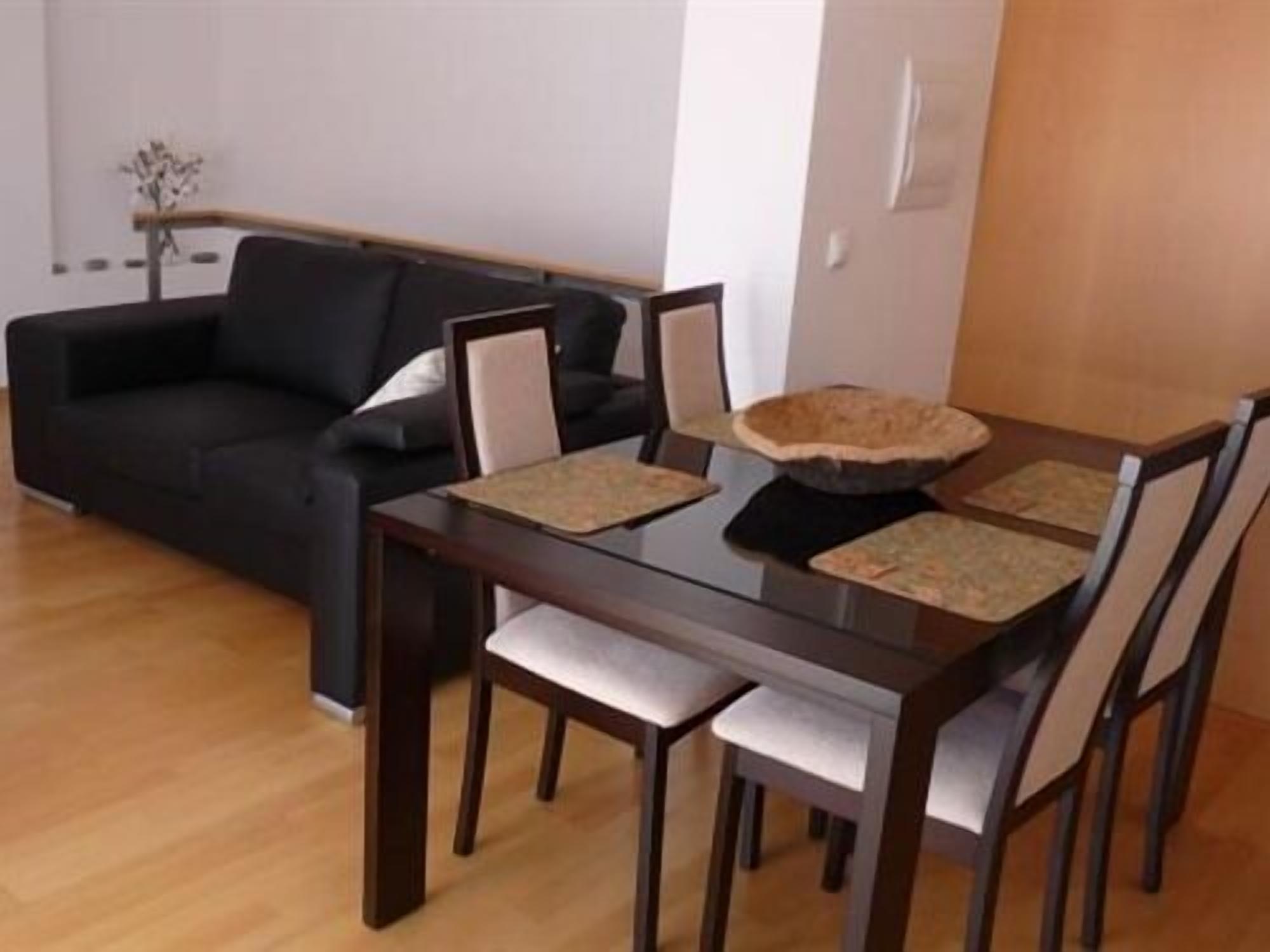 A dining area with a dark wooden table and chairs, a black sofa, and a decorative bowl on the table.