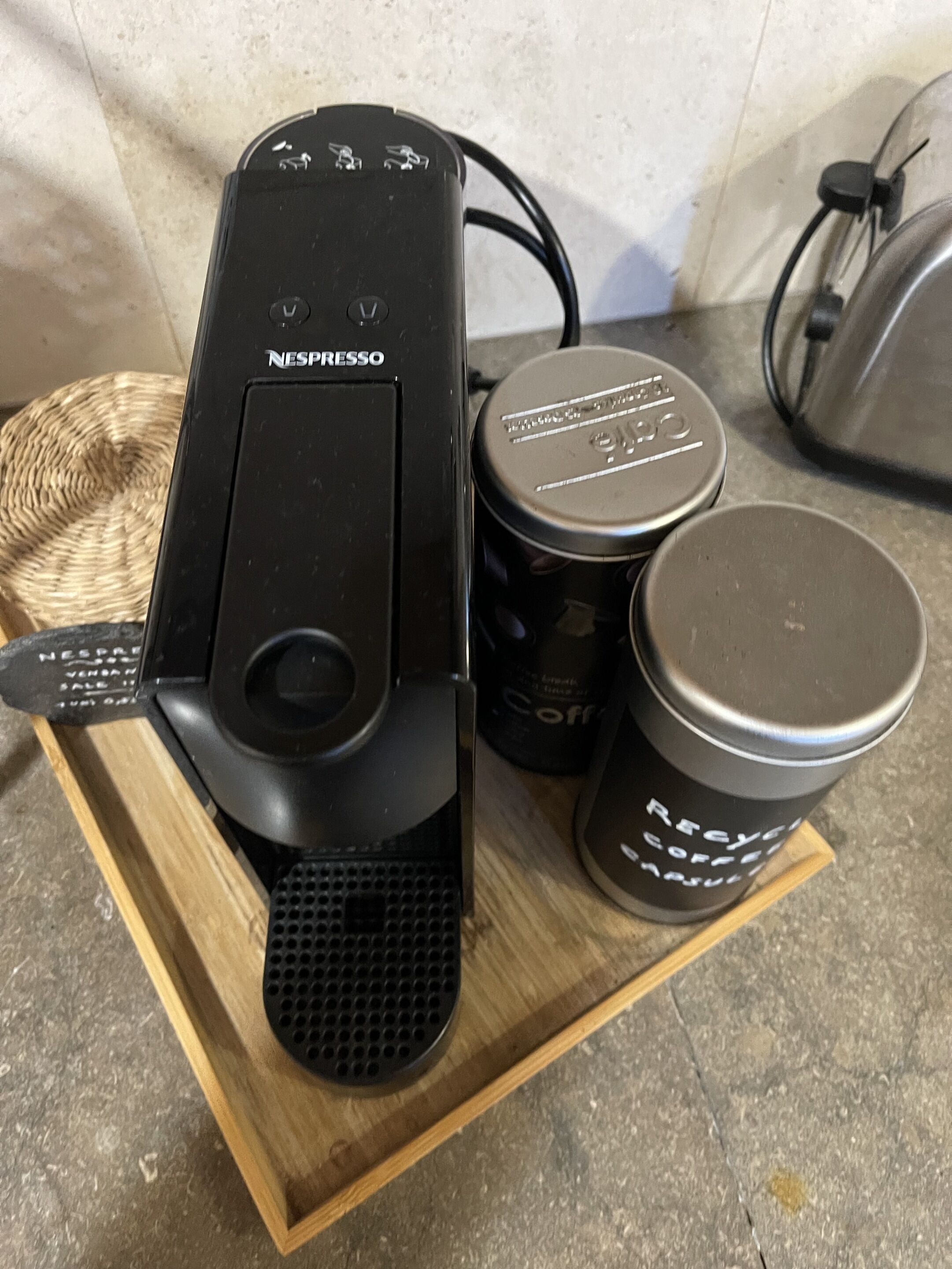 Une machine à café Nespresso posée sur un plateau en bois, avec une tasse réutilisable et une capsule de café.
