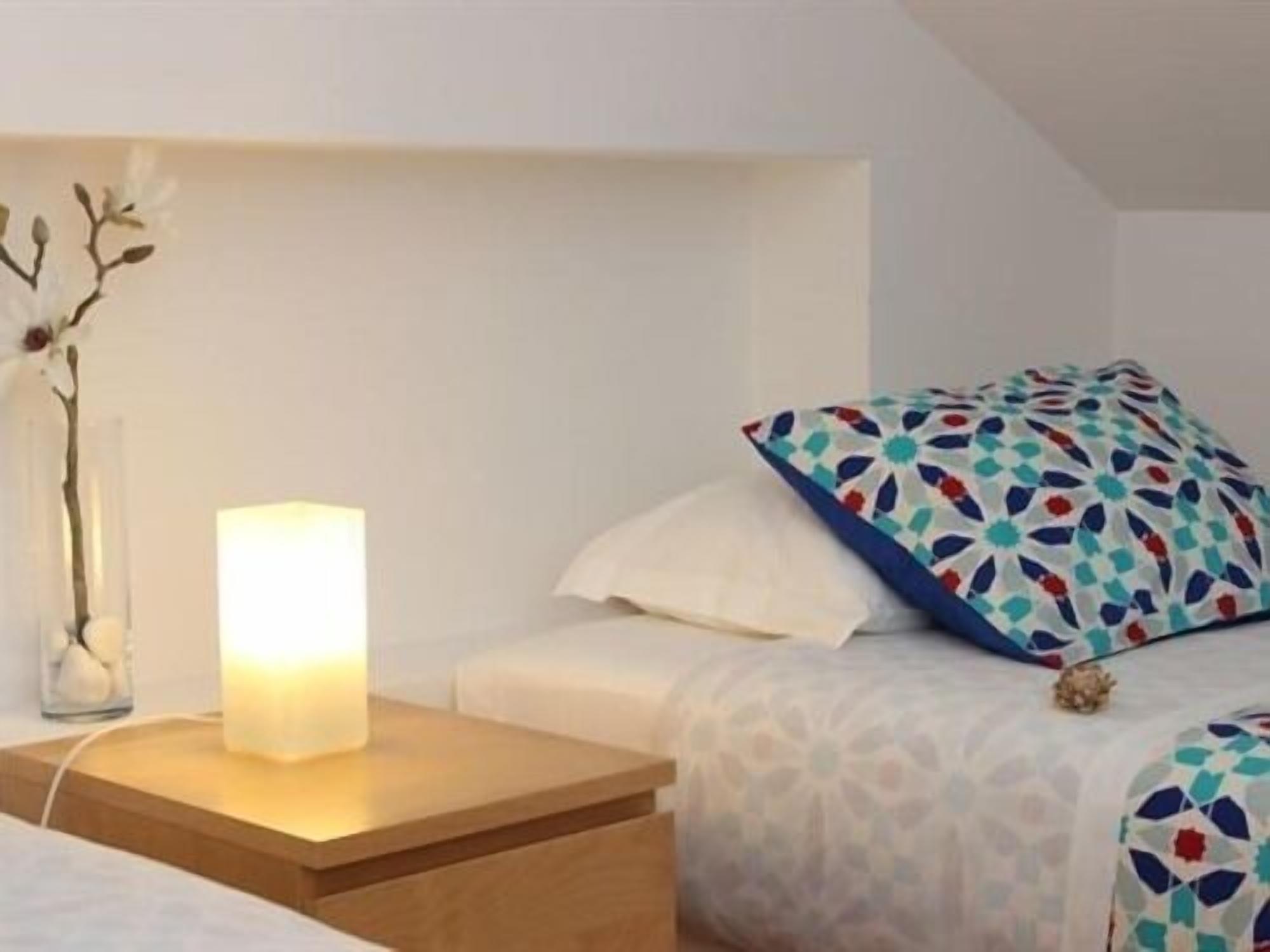 A hotel room with a bed, a bedside table with a lamp, and a decorative vase with branches.