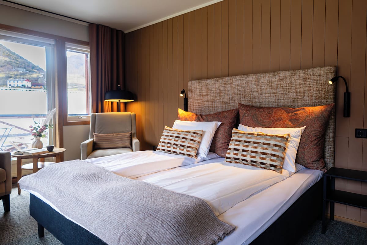 Habitación de hotel con una cama grande, una silla, una mesita y vistas al exterior.