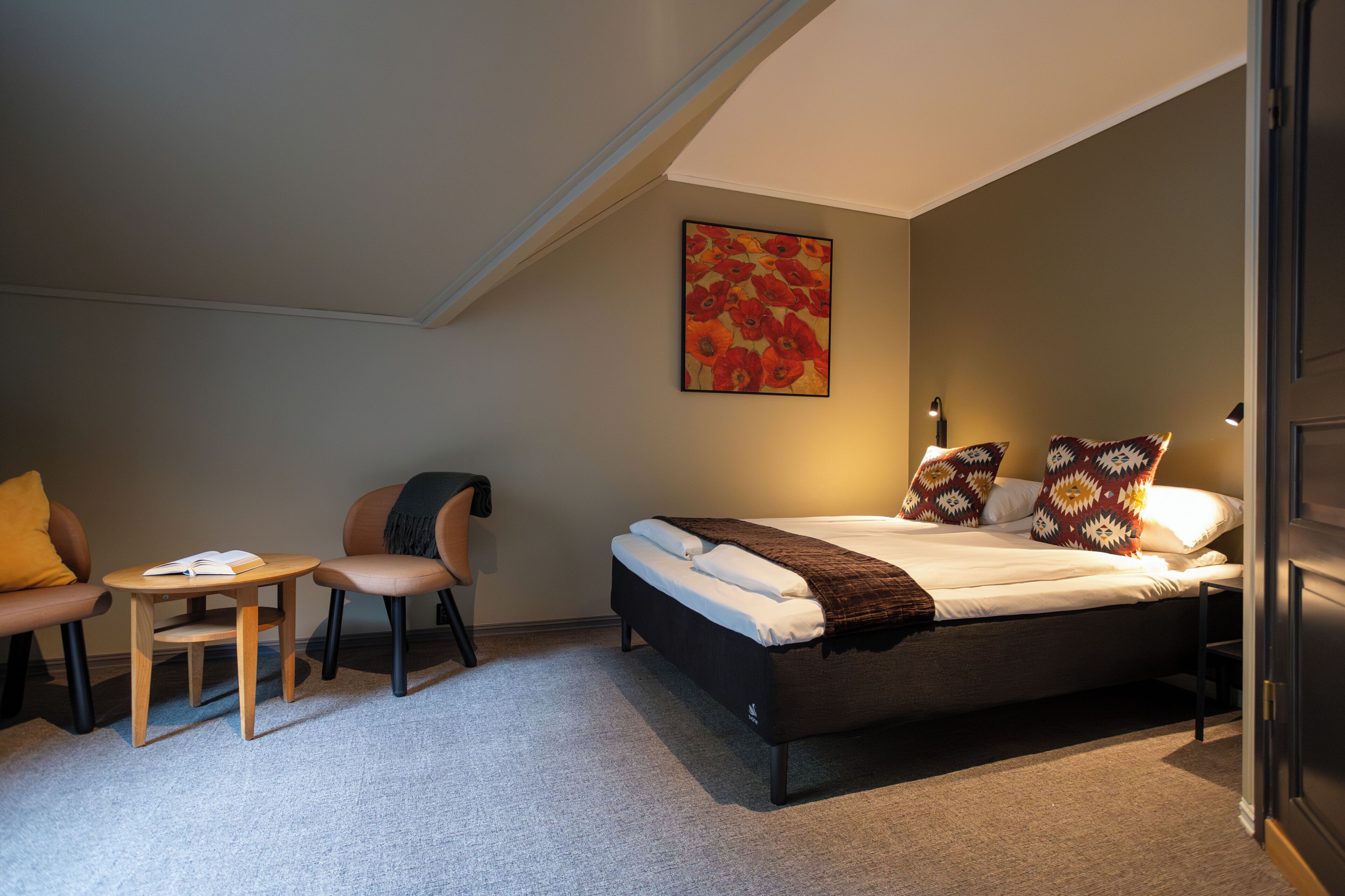 Een slaapkamer met een bed, een stoel, een klein tafeltje en een schilderij aan de muur.