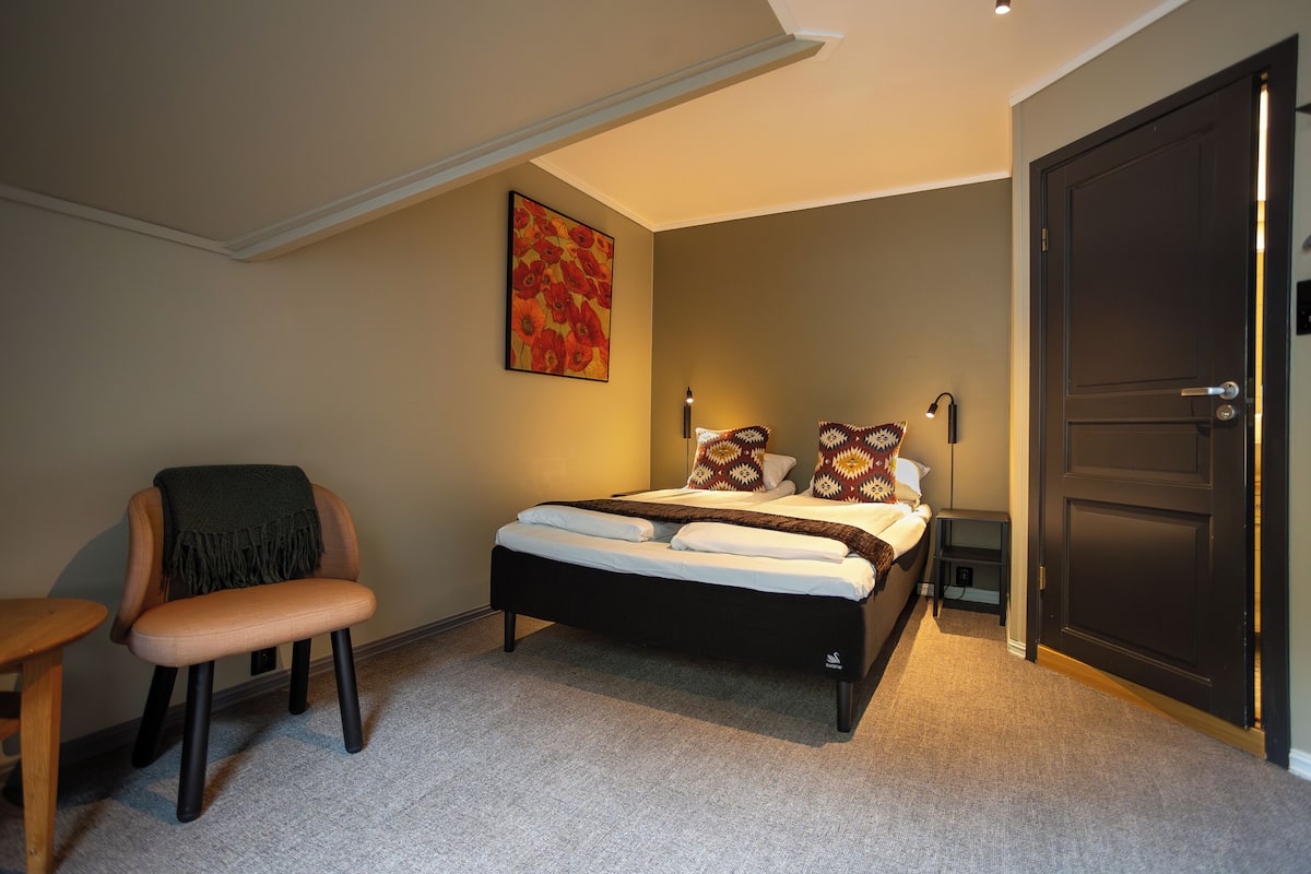Un dormitorio con cama, una silla, una puerta y un cuadro en la pared.