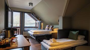 Una habitación de hotel moderna con dos camas, un área de comedor con mesa y sillas, y ventanas grandes que ofrecen vistas al exterior.