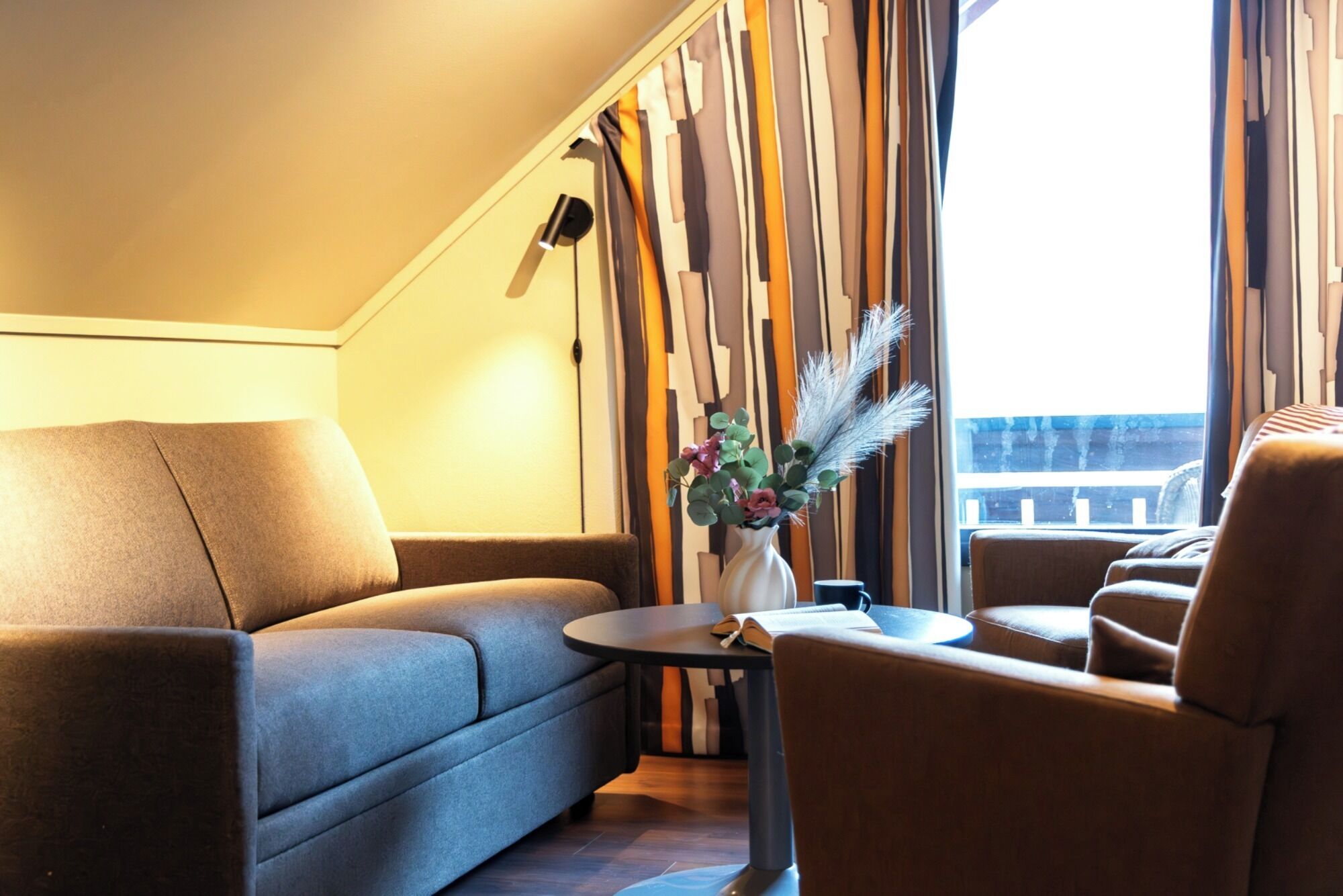 Ein modernes Wohnzimmer mit einer Couch, einem Sessel und einem kleinen Tisch mit einem Blumenstrauß.
