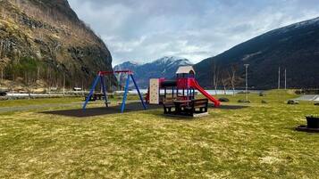 Explore the great outdoors at this playground surrounded by a lush green field and majestic mountains.