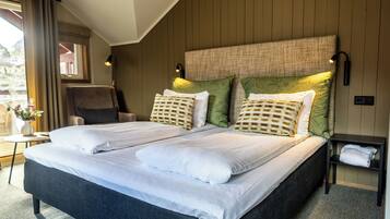 A double bed with white linens, a headboard with a textured pattern, two wall-mounted reading lamps, and a small bedside table with a folded towel.