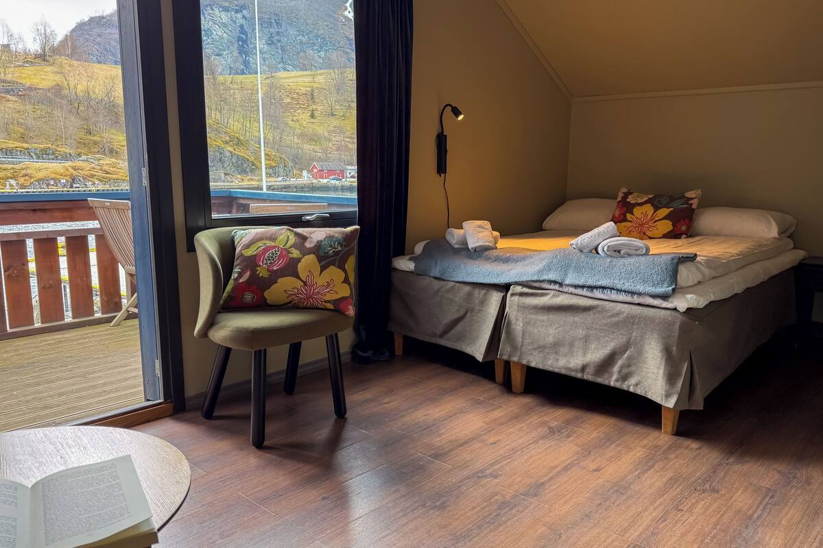 Un dormitorio con una cama, una silla, una mesa con un libro y vistas a un paisaje.