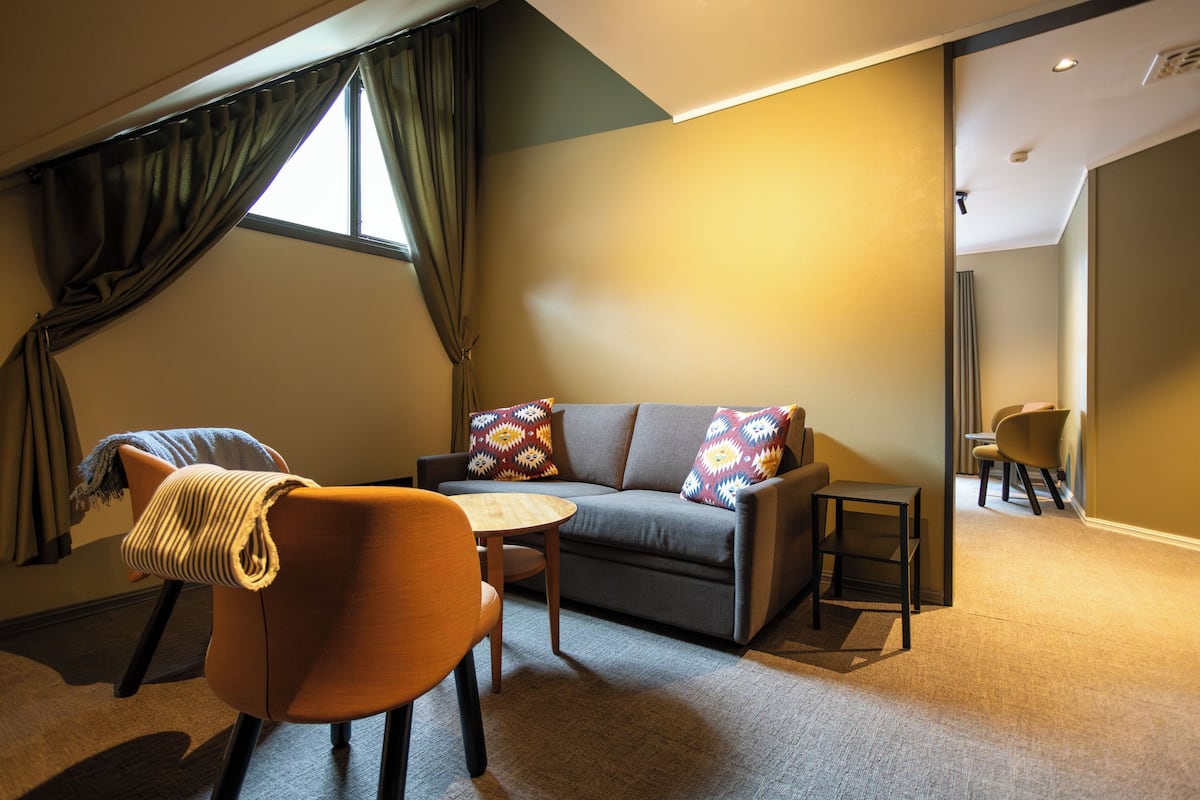 Una sala de estar moderna con un sofá, un sillón, una mesita y vistas a un paisaje urbano a través de una ventana.