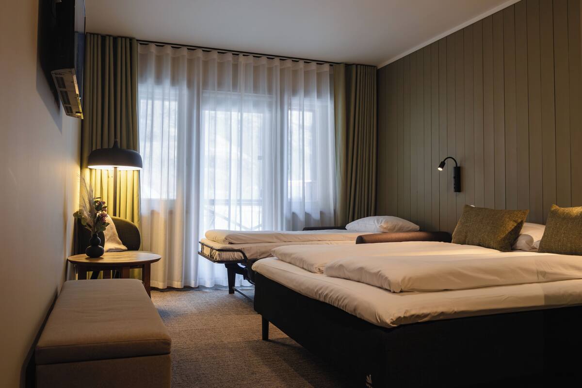 Habitación de hotel con dos camas, un escritorio, una silla, una lámpara y una ventana con cortinas.
