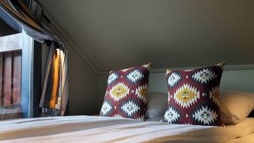 A bed with white bedding, two patterned pillows, and a window with curtains.