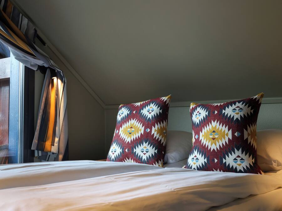 A bed with white bedding, two patterned pillows, and a window with curtains.