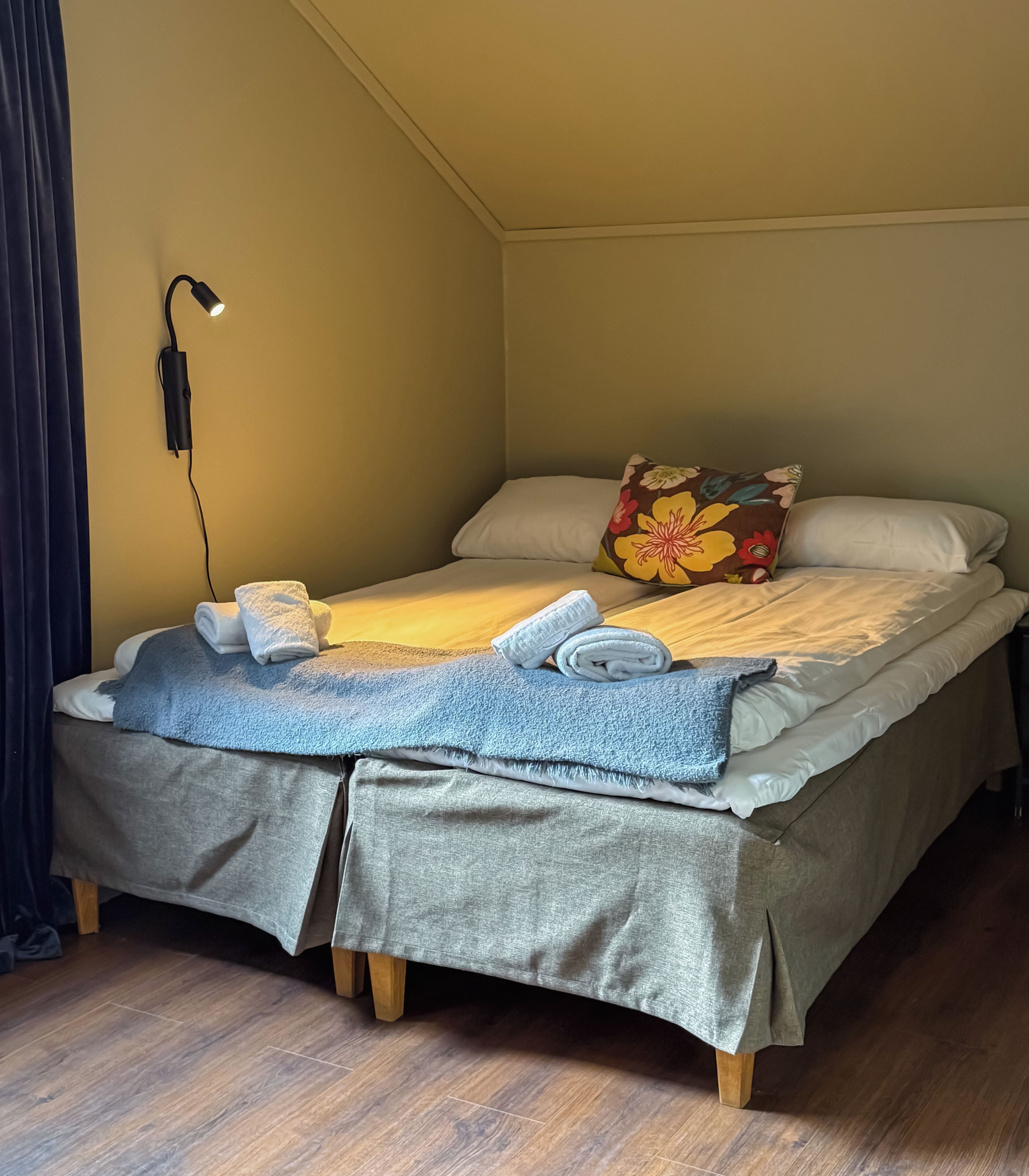 A bed with a grey bedspread, a blue towel, and a floral pillow.