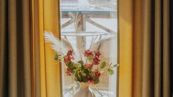 Una habitación con una mesa redonda, un jarrón con flores y vistas a través de una ventana con cortinas.