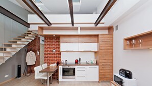 A modern kitchen with white cabinets, a brick accent wall, a dining area with a wooden table and white chairs, and a built-in oven. - EchoDom 3 Apartments (Kraków)