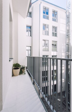 A narrow balcony with a metal railing, potted plants, and a view of a white building with multiple windows. - EchoDom 3 Apartments (Kraków)
