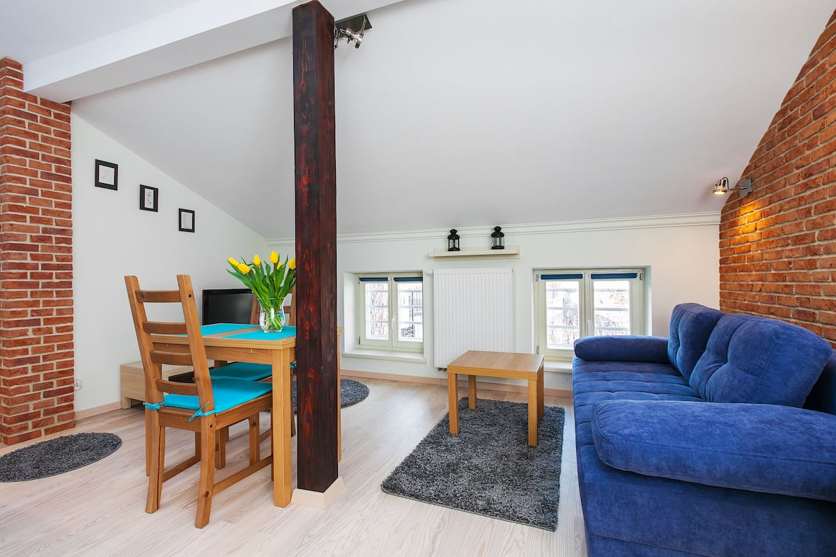 Uma sala de estar aconchegante com uma mesa de jantar de madeira, cadeiras, um sofá azul e uma lareira.