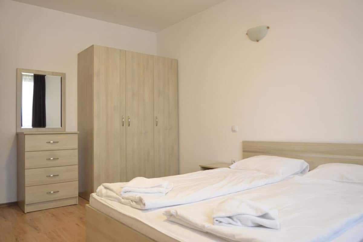 A bedroom with a bed, a wardrobe, a mirror, and a nightstand.
