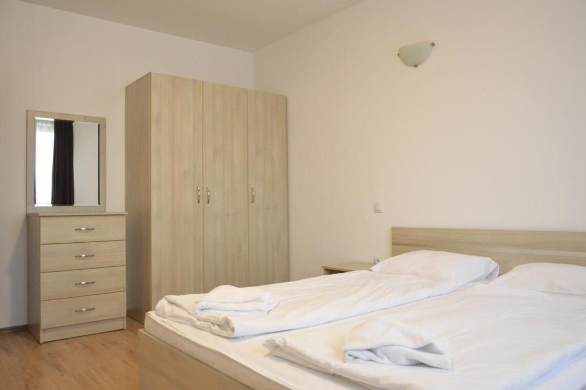 Quarto com cama, guarda-roupa, espelho e mesa de cabeceira.