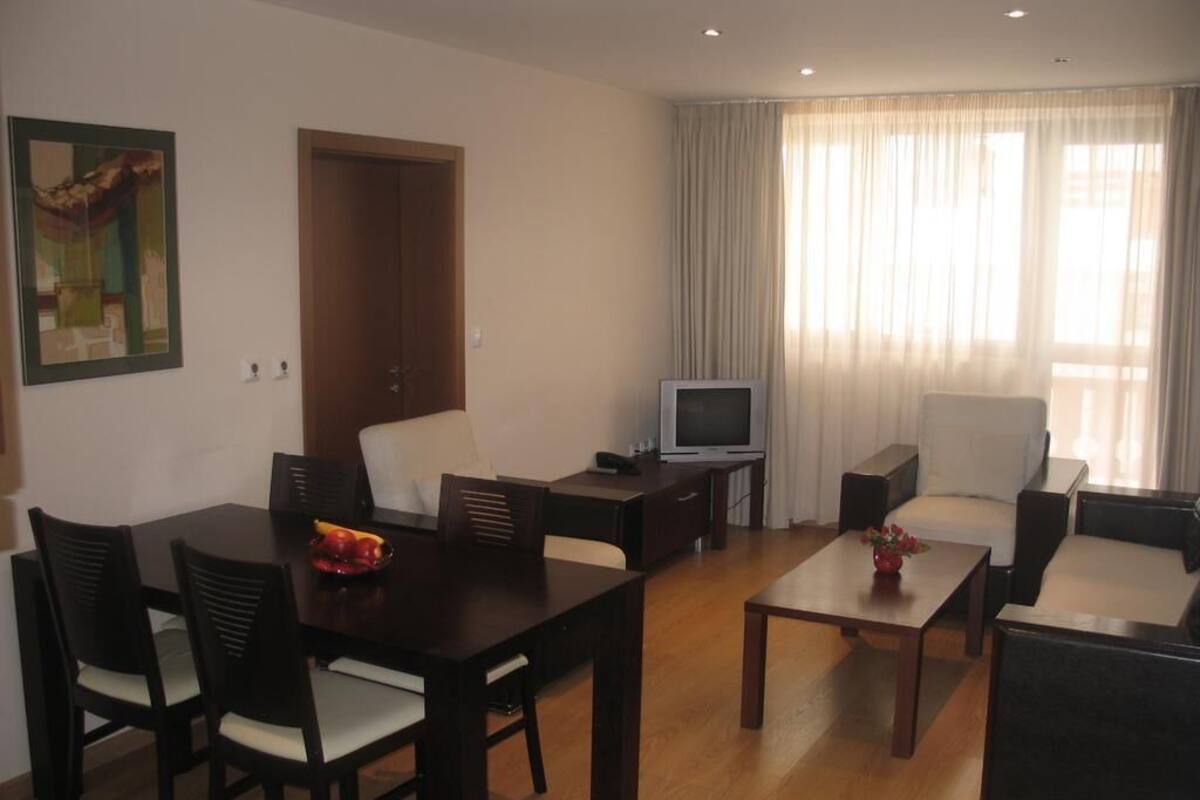 A living room with a dining table, chairs, a sofa, a TV, and a door.