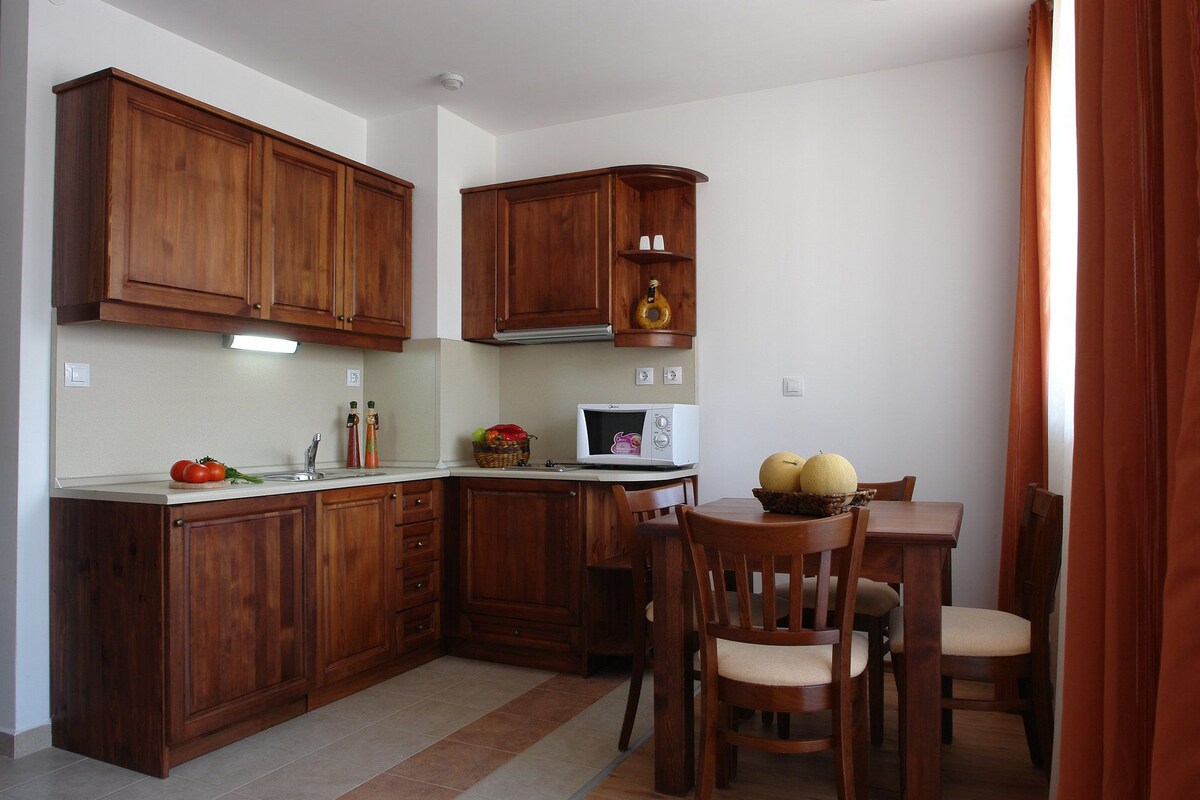 Cozinha compacta com armários de madeira, micro-ondas e área de refeições com cadeiras.