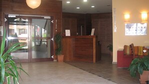 Et receptionsområde med en træreception, en glasdør og et rødt siddeområde med plantekrukker.
