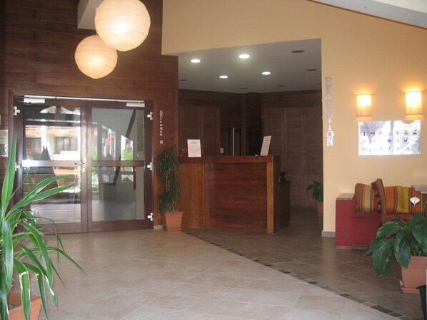 A reception area with a wooden reception desk, a glass door entrance, and a red seating area with potted plants.