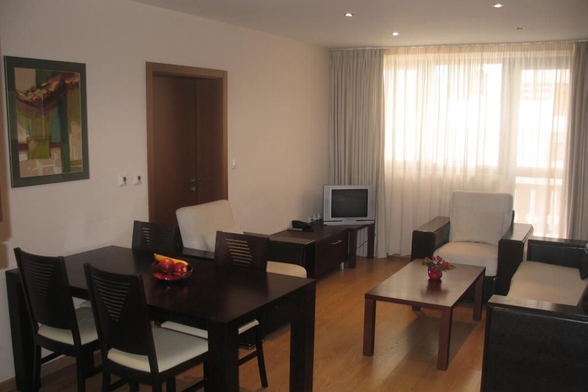 A living room with a dining table, chairs, a sofa, a TV, and a door.