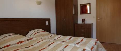 Quarto com cama, guarda-roupa, espelho e porta.