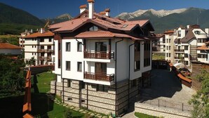 A multi-story building with balconies, a stone base, and a view of mountains in the background. - Winslow Elegance Hotel (Bansko)