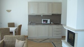 A modern living room with a sofa, a dining table, and chairs. A kitchen with cabinets and a microwave is visible in the background. - Winslow Elegance Hotel (Bansko)