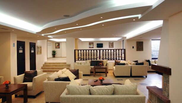 A spacious living area with multiple sofas and a fireplace, featuring a modern ceiling design and a staircase leading to an upper level. - Winslow Elegance Hotel (Bansko)
