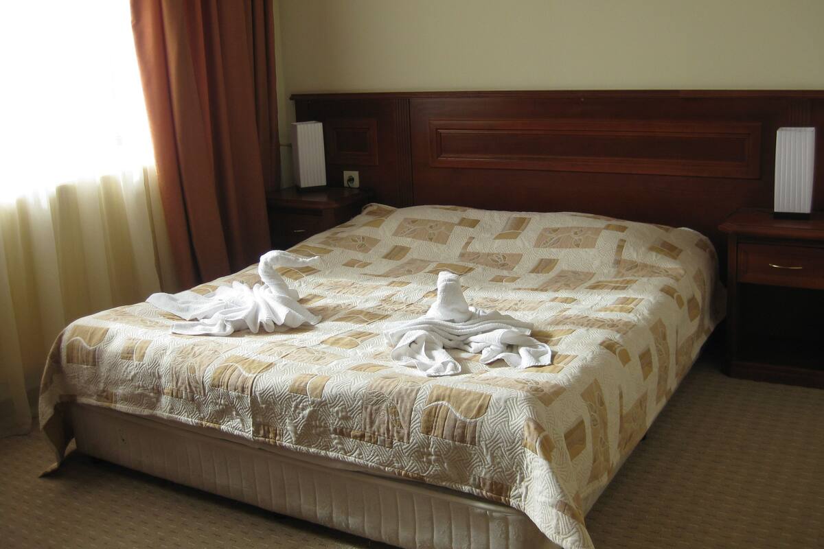 A hotel room with a large bed, wooden headboard, and a nightstand with a lamp.