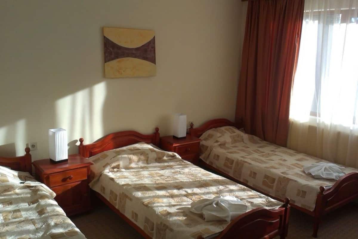 A room with two single beds, wooden headboards, a bedside table with a lamp, and a wall-mounted abstract painting.
