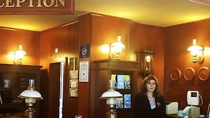 A reception area with a wooden reception desk, two wall-mounted lamps, a clock, and a sign that reads "RECEPTION". - Hotel Elina (Chepelare)