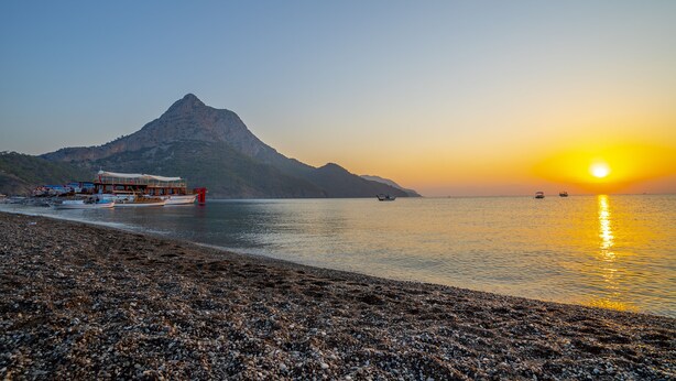 Una playa de guijarros con barcos, una montaña y un atardecer.