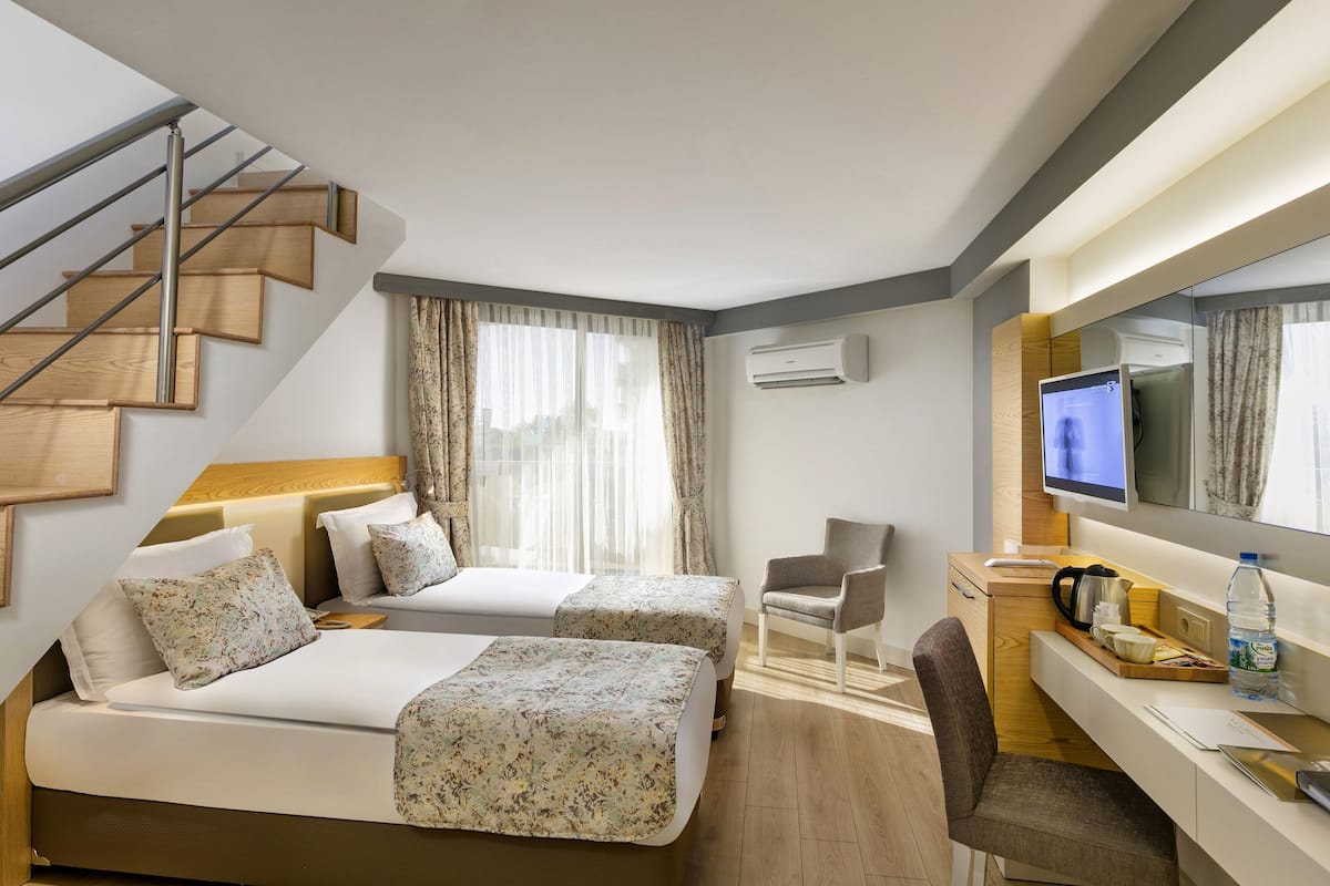 A hotel room with two beds, a desk, a chair, a TV, and a staircase.
