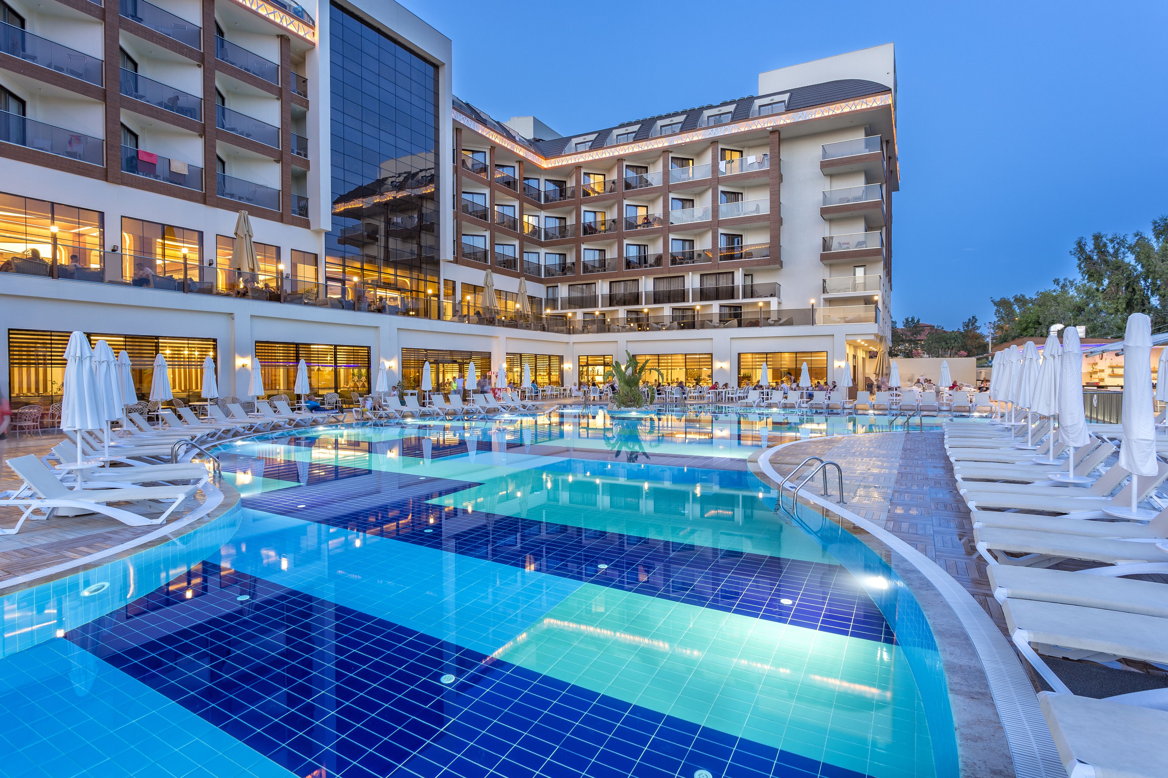 A hotel with a large indoor swimming pool, multiple balconies, and outdoor seating areas.